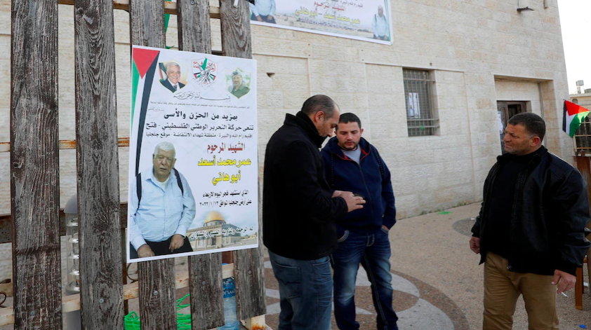 Los hombres se paran junto a un cartel del palestino Omar Abdalmajeed As'ad, de 80 años, en la aldea de Jiljilya en Cisjordania (Crédito: MOHAMAD TOROKMAN/REUTERS)