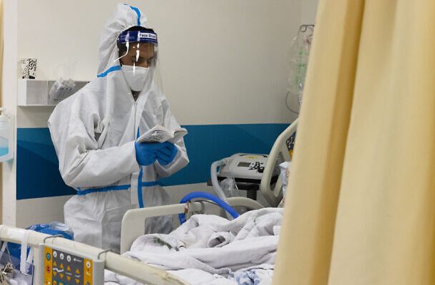 El hijo de un paciente diagnosticado con COVID-19 lee salmos junto a la cama de su padre en el hospital Shaare Zedek de Jerusalén el 20 de enero de 2022. (Olivier Fitoussi/Flash90)