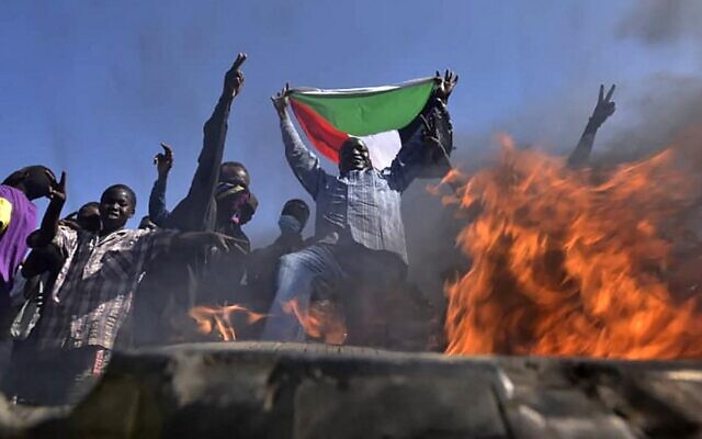Un hombre sostiene una bandera nacional sudanesa ante las llamas en una barricada mientras la gente protesta contra el golpe militar en Sudán, en el este de la capital, Jartum, el 13 de noviembre de 2021. (AFP)