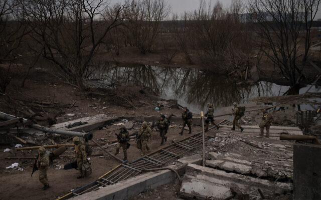 Soldados ucranianos cruzan un camino improvisado debajo de un puente destruido en Irpin, en las afueras de Kiev, Ucrania, el 12 de marzo de 2022. (AP/Felipe Dana)