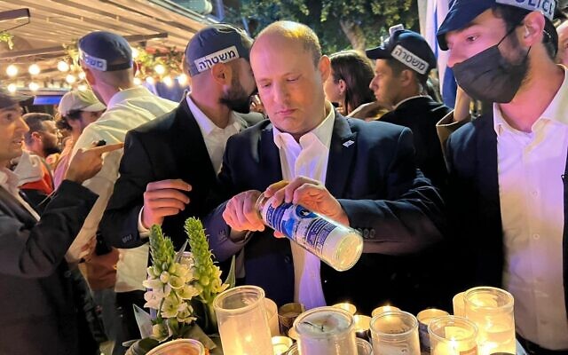 El primer ministro Naftali Bennett enciende una vela conmemorativa mientras asiste a la reapertura del bar Ilka de Tel Aviv días después de que fuera atacado en un ataque terrorista, el 11 de abril de 2022 (Cortesía)