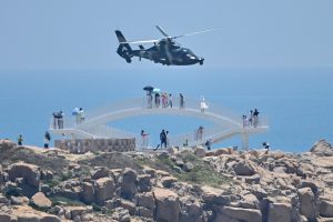 Radio Jai -Los turistas observan cómo un helicóptero militar chino pasa volando por la isla de Pingtan, uno de los puntos más cercanos de China continental a Taiwán
