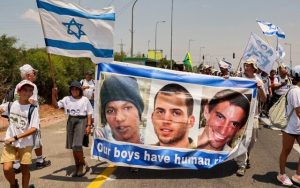 Radio Jai -Archivo: Manifestantes que marchan con una pancarta que muestra los rostros de la civil israelí cautiva Avera Mengistu, y los soldados fallecidos Oron Shaul y Hadar Goldin de la ciudad israelí de Ashkelon llegan al kibutz de Karmia el 5 de agosto de 2022. (JACK GUEZ / AFP)